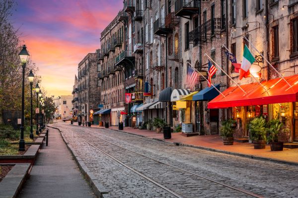Picture of famous River Street, in Savannah, Georgia.  Railroad tracks running past storefronts, along a road lined with cobblestone pavers.