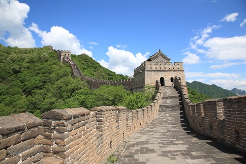 Photo of the Great Wall of China.  Close up of bricks in the foreground, and the wall extending up a green hill in the background.
