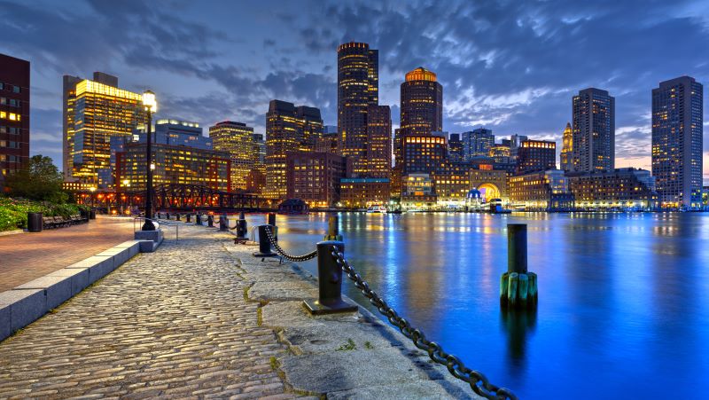 The Boston skyline at dusk.  A path along the bay made from cobblestone pavers.