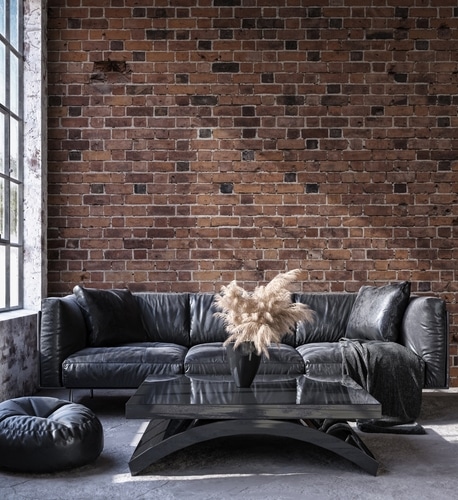photo of a modern living room, with a reddish thin brick veneer wall in the background, and a black couch in the foreground.