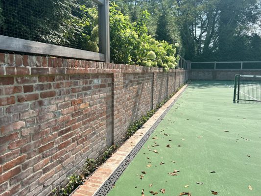 A reclaimed brick wall built around a home tennis court.