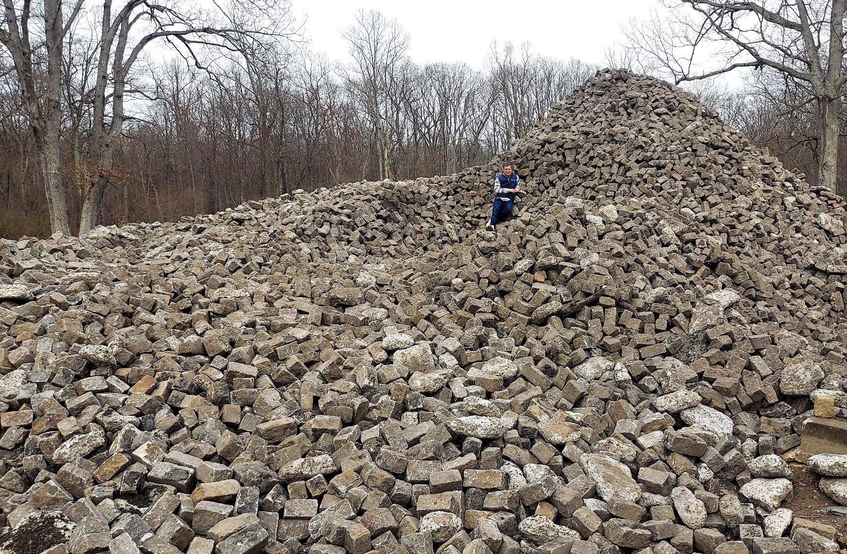 Granite cobblestones in a huge pile, with a person standing halfway up the pile, in order to emphasize the size of the pile.