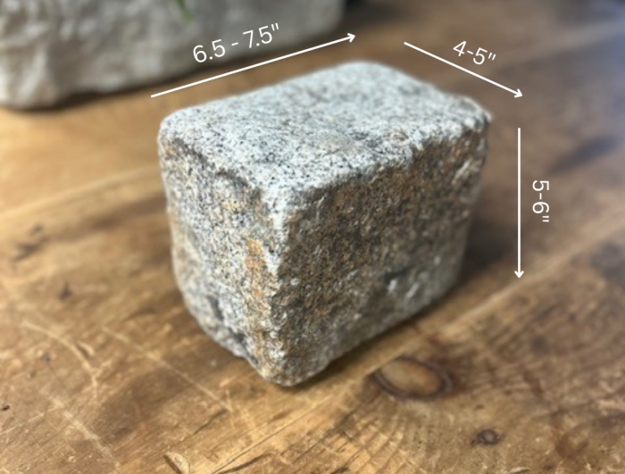Close-up of a granite cobble placed on a table, with dimensions superimposed for reference.