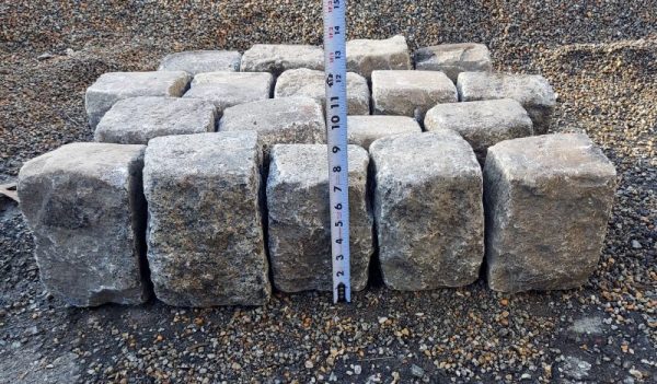 Granite cobbles staged to stand with their longest side vertical, and a tape measure placed in front to display their height.