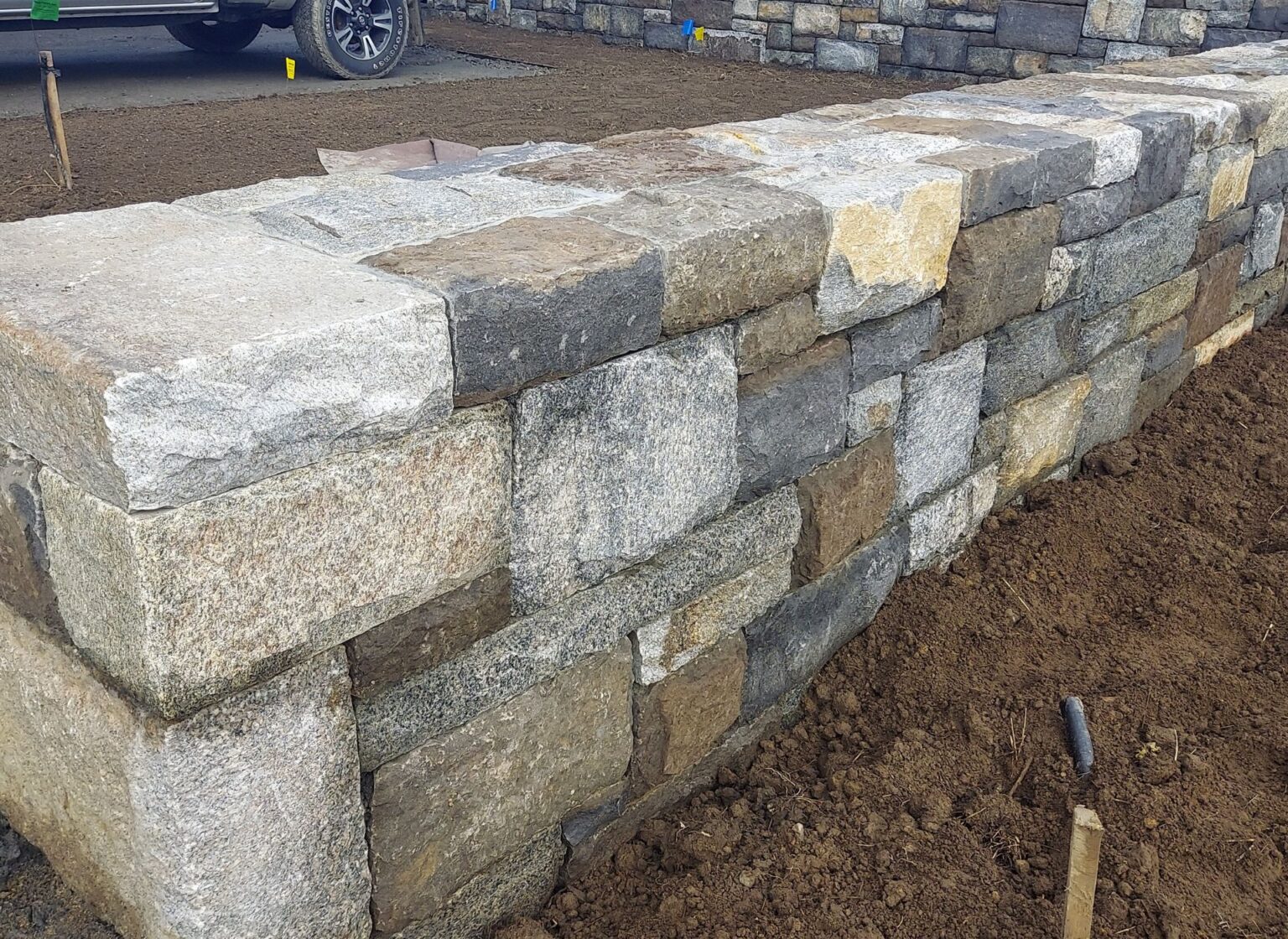 A landscape retaining wall built in an ashlar pattern using reclaimed stone, featuring rectangular blocks with varied tones during installation.
