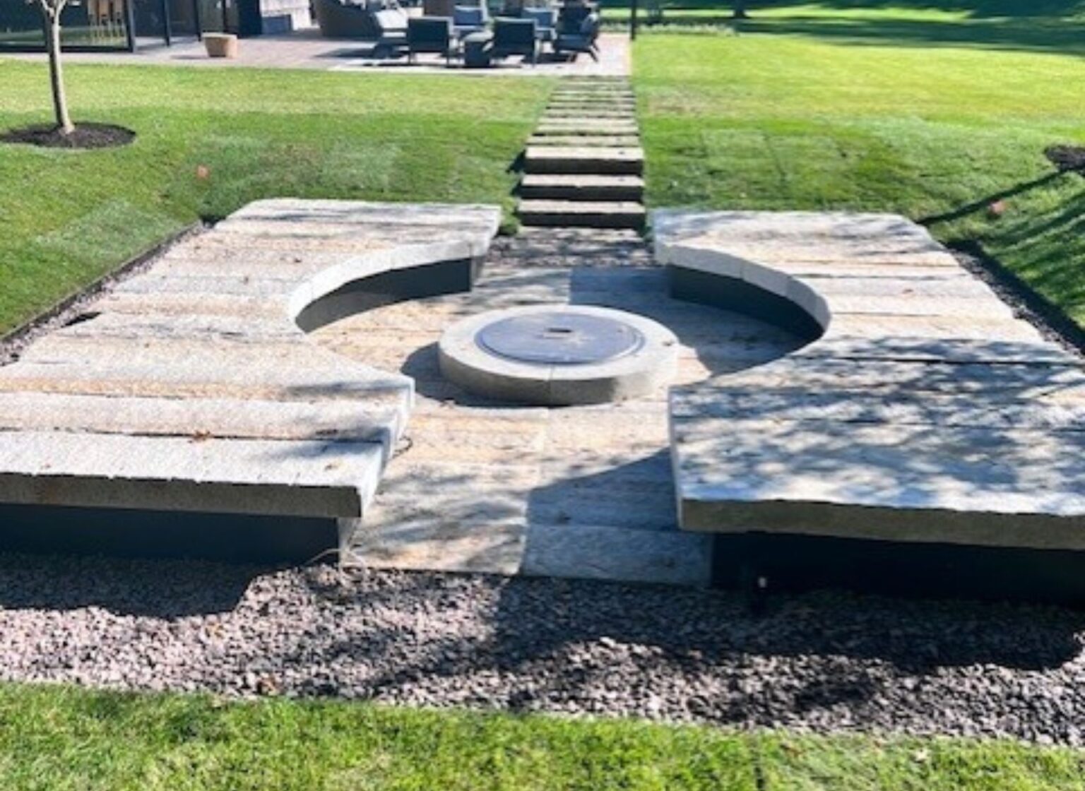 A circular stone firepit sitting atop granite planks, with granite plank seating cut into a a larger circle surrounding the firepit.