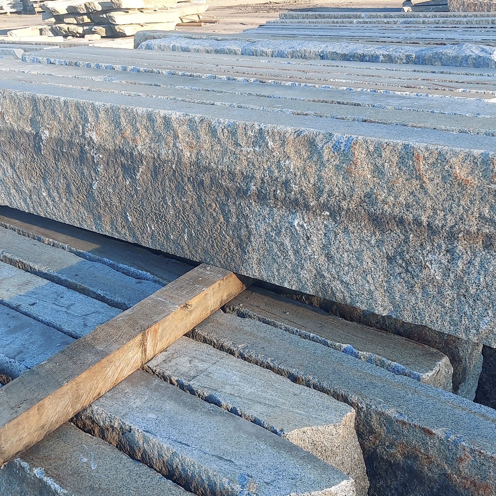 long pieces of paving grade reclaimed granite curbing with sawn edges, stacked neatly in rows