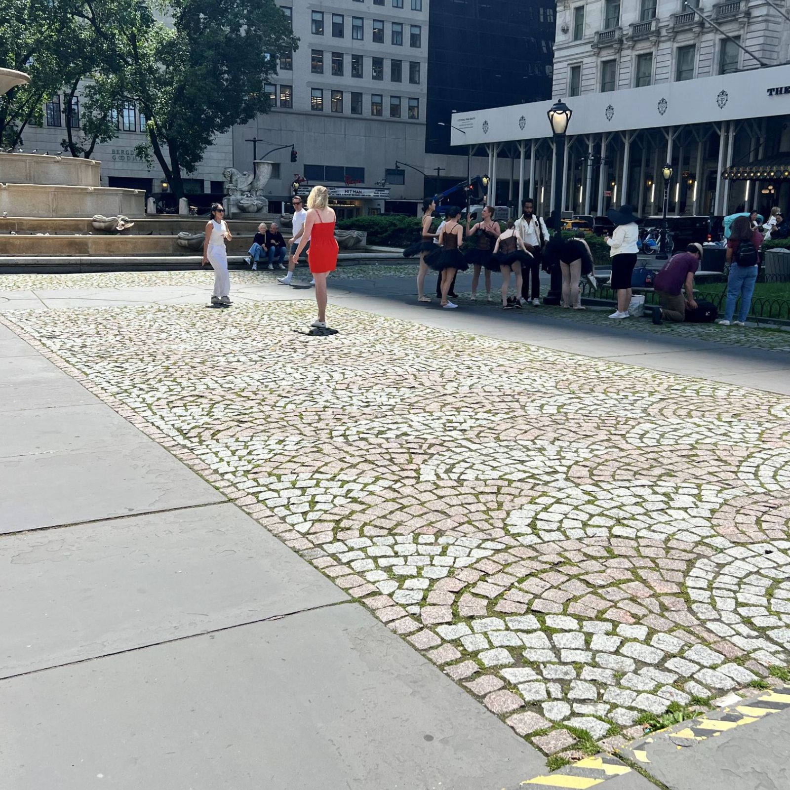 A city plaza, with cobblestone cubes and bluestone sidewalk. People are seen walking in the background.