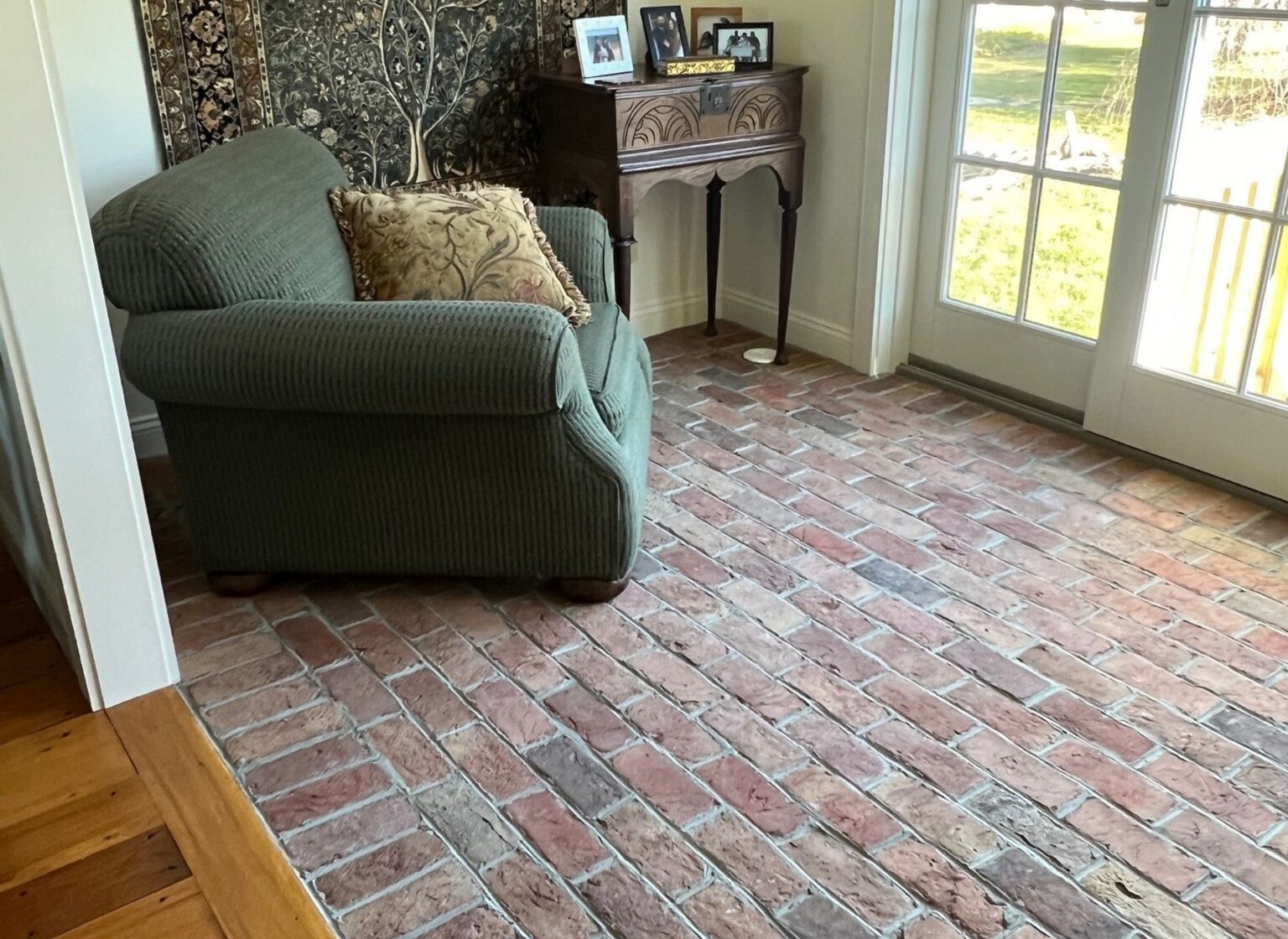 Sunroom with a reclaimed brick floor and a green chair facing the French doors.