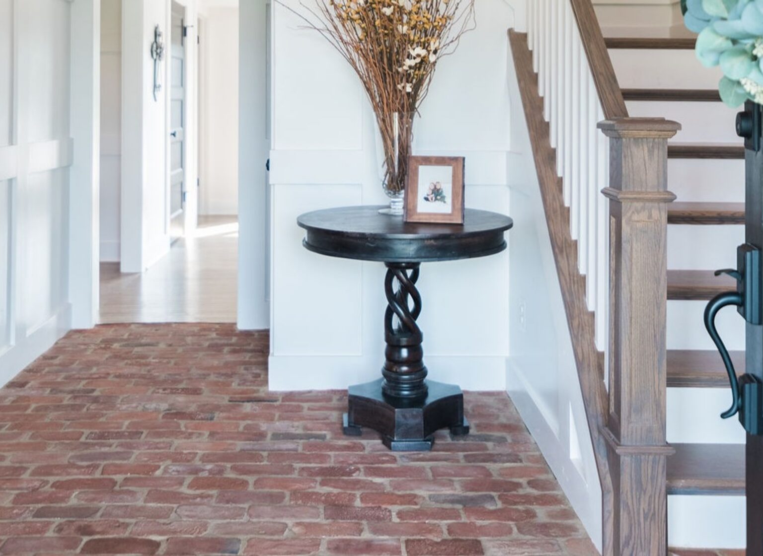 Foyer with antique brick tile floor and a small side table below the stairs.