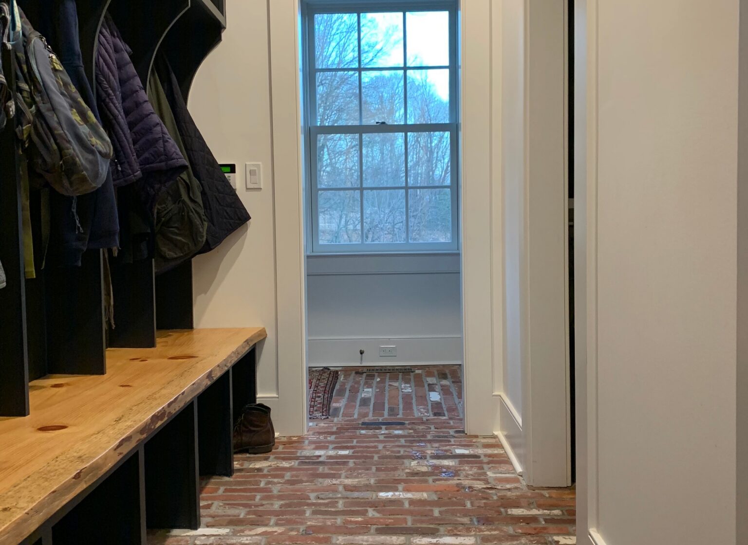 Mudroom with antique brick tile floor. There is a door at the end of the space.