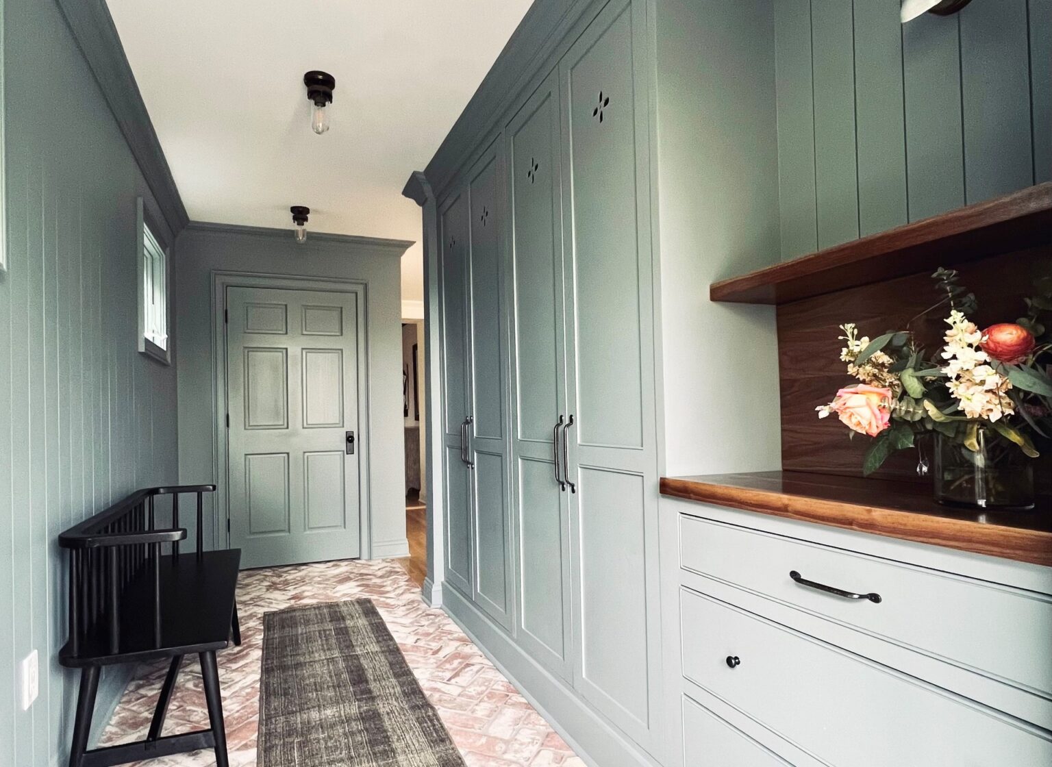 Mudroom with reclaimed brick tile floor and green wall panels.
