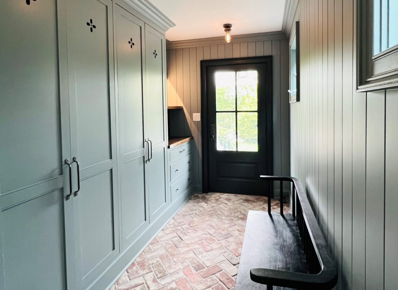 Mudroom with reclaimed brick tile floor and green wall panels.