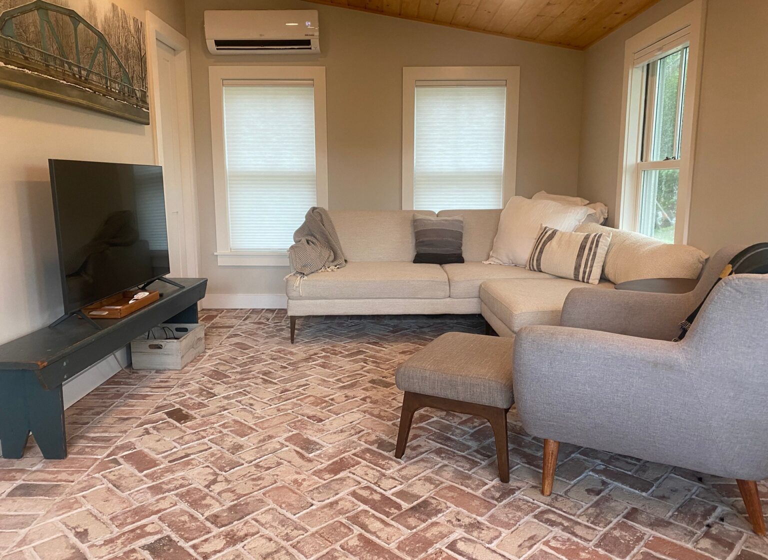 Living room with reclaimed herringbone brick flooring, featuring a couch, chair, and TV.