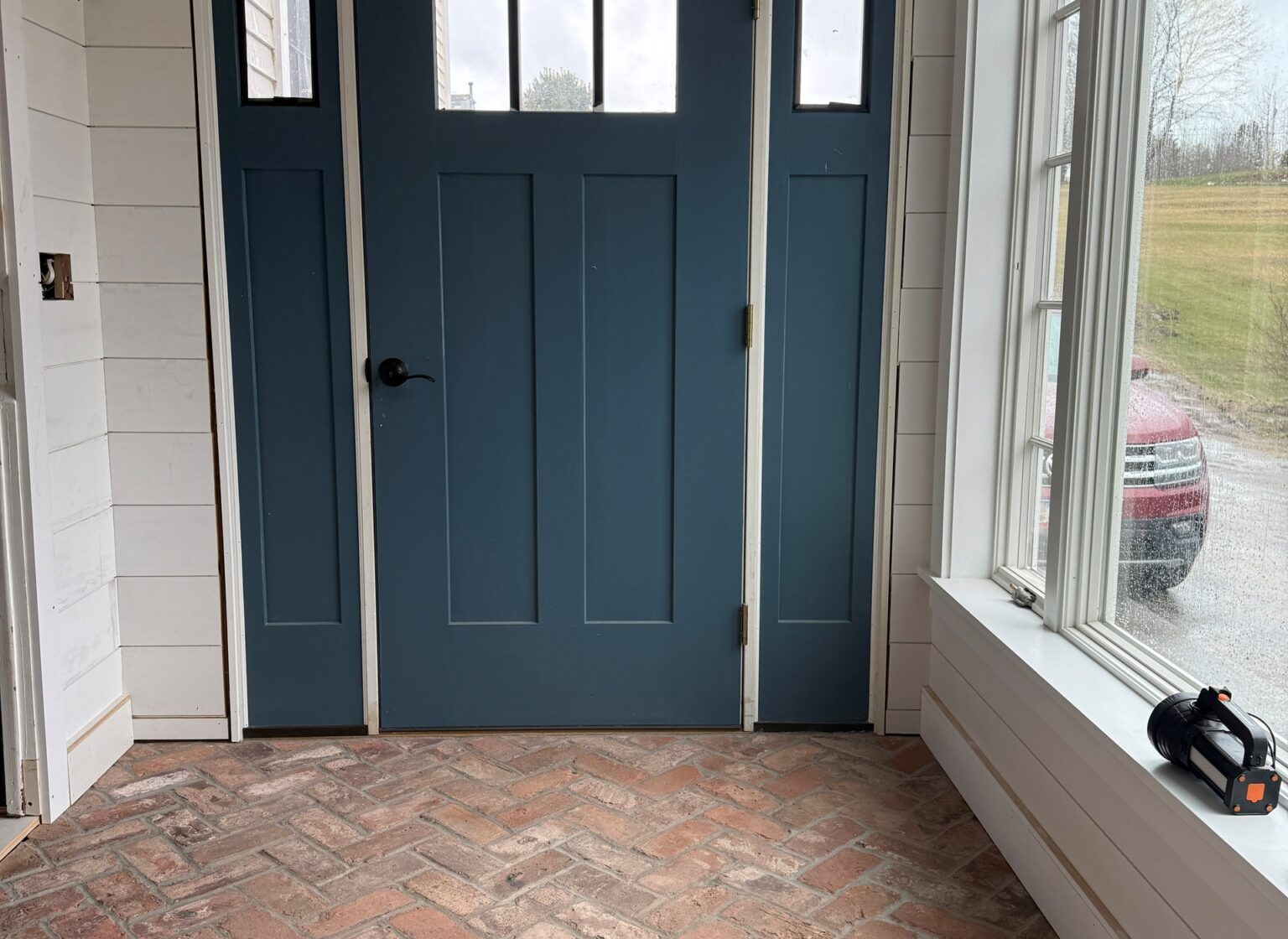 Reclaimed herringbone brick floor entryway with blue door.