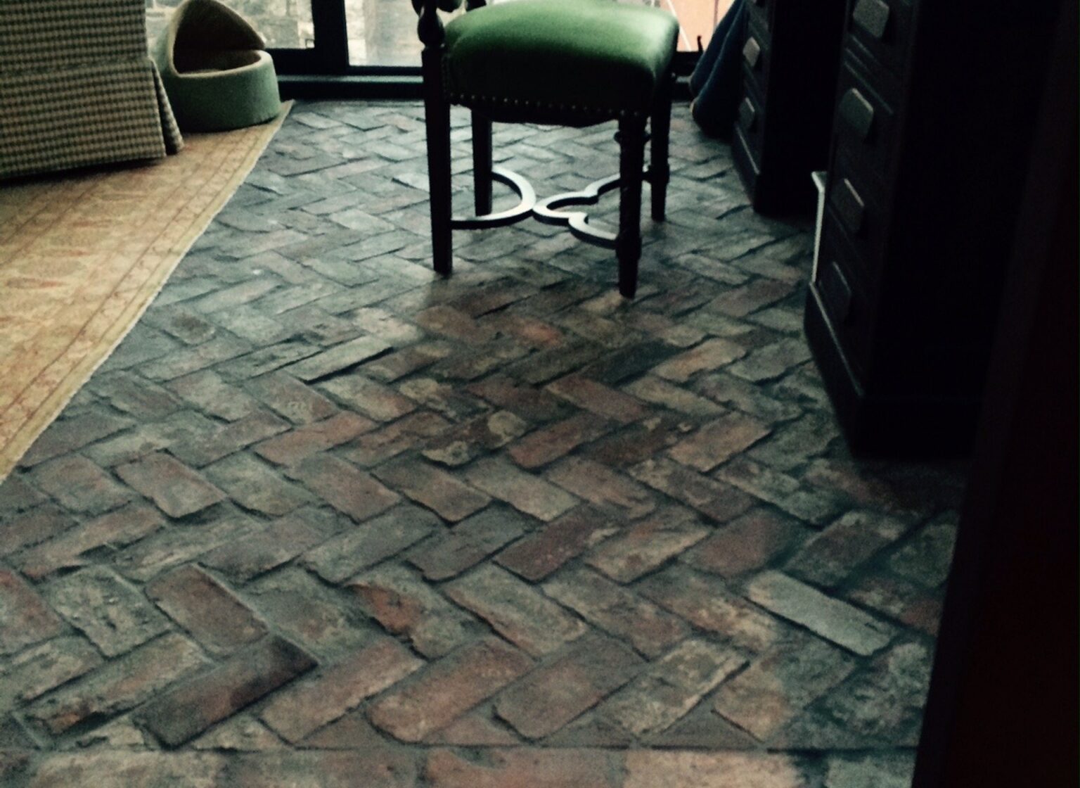 Reclaimed brick tile floor with a green chair in the center of the room.