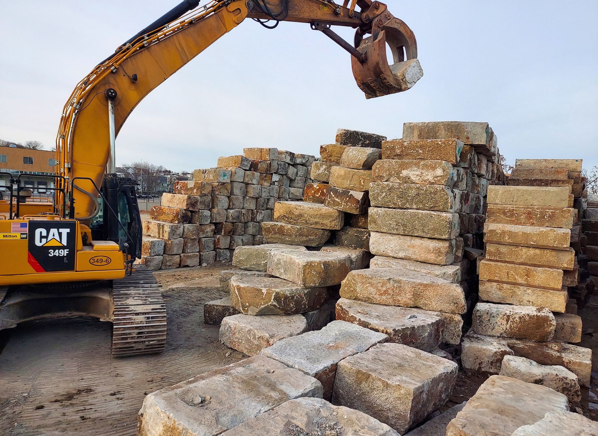 Reclaimed granite blocks stacked in the Stone Farm yard with an excavator